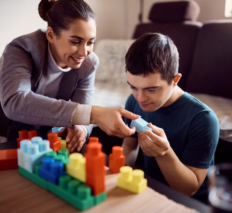 Man with down syndrome enjoying while stacking toy blocks with his psychologist at home. Portsmouth PBS Network.